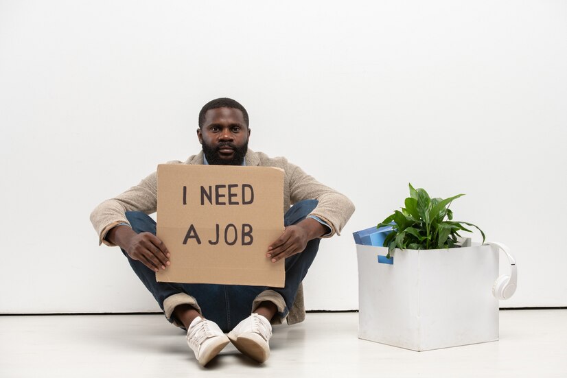 young-jobless-man-african-ethnicity-with-piece-cardboard-saying-that-he-needs-job-sitting-floor-by-white-wall-office_274679-14838
